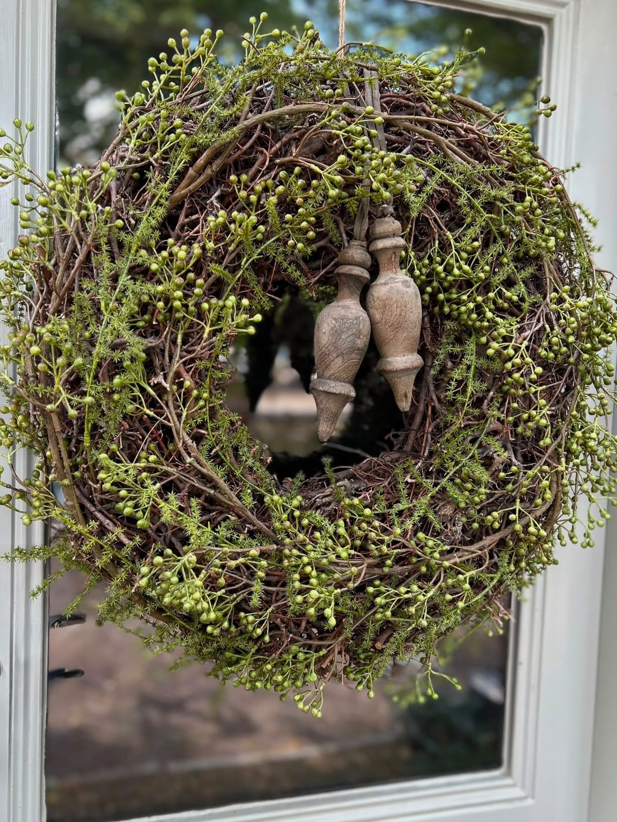 Krans van groene besjes en takken van Art de la Fleur, met houten ornamenten in het midden