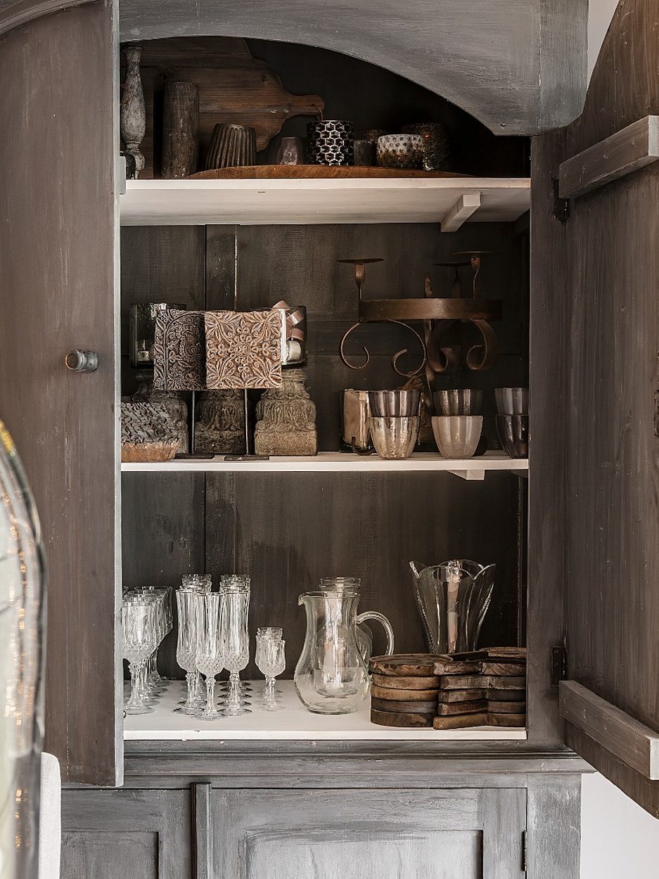 Antieke kast met open deuren, gevuld met oud glaswerk en aardewerk