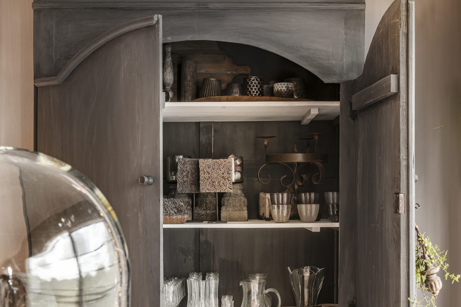 Open houten vitrinekast met oud glaswerk, stolp en verzamelstukken van de Atelierselectie