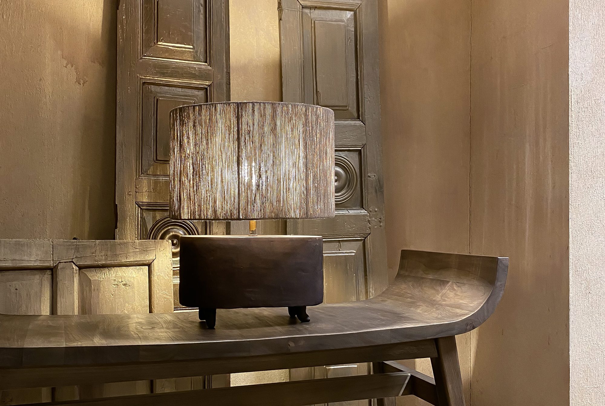 Hoffz-sidetable in doorleefd hout met linnen lampen, tegen een wand van oude paneeldeuren