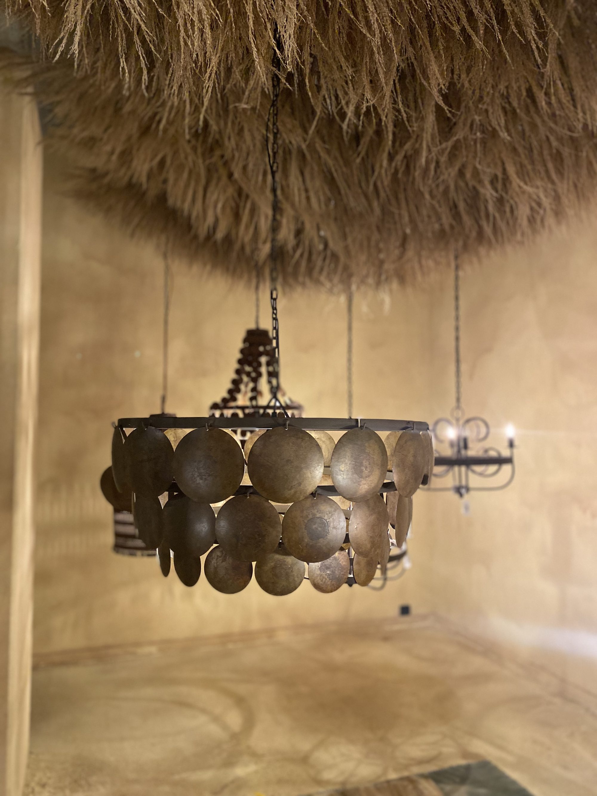 Ronde kroonluchter met metalen schijfjes onder een plafond van ruw riet