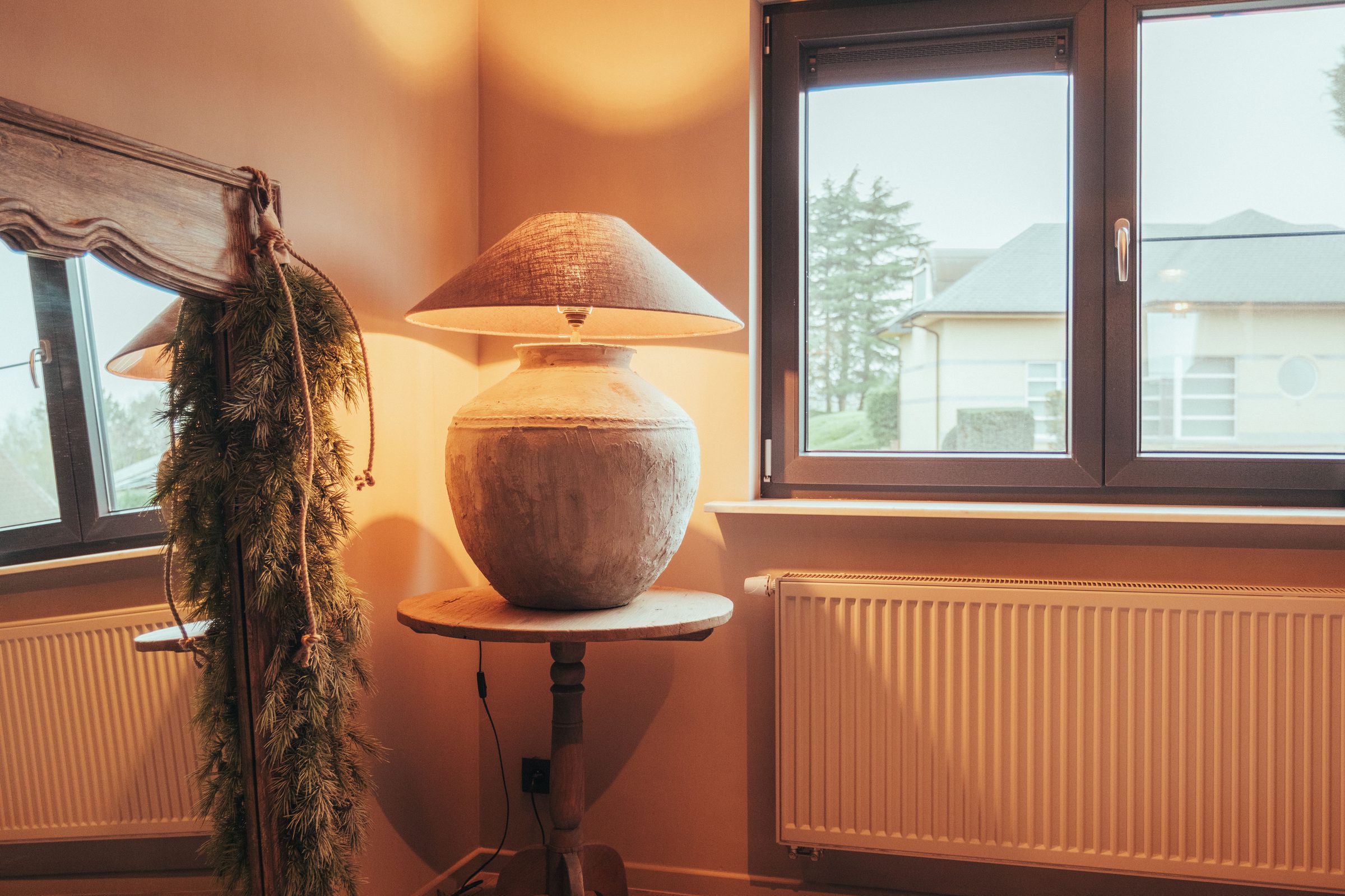 Terracotta kruikenlamp bij het raam met dennentak — Nina 2025
