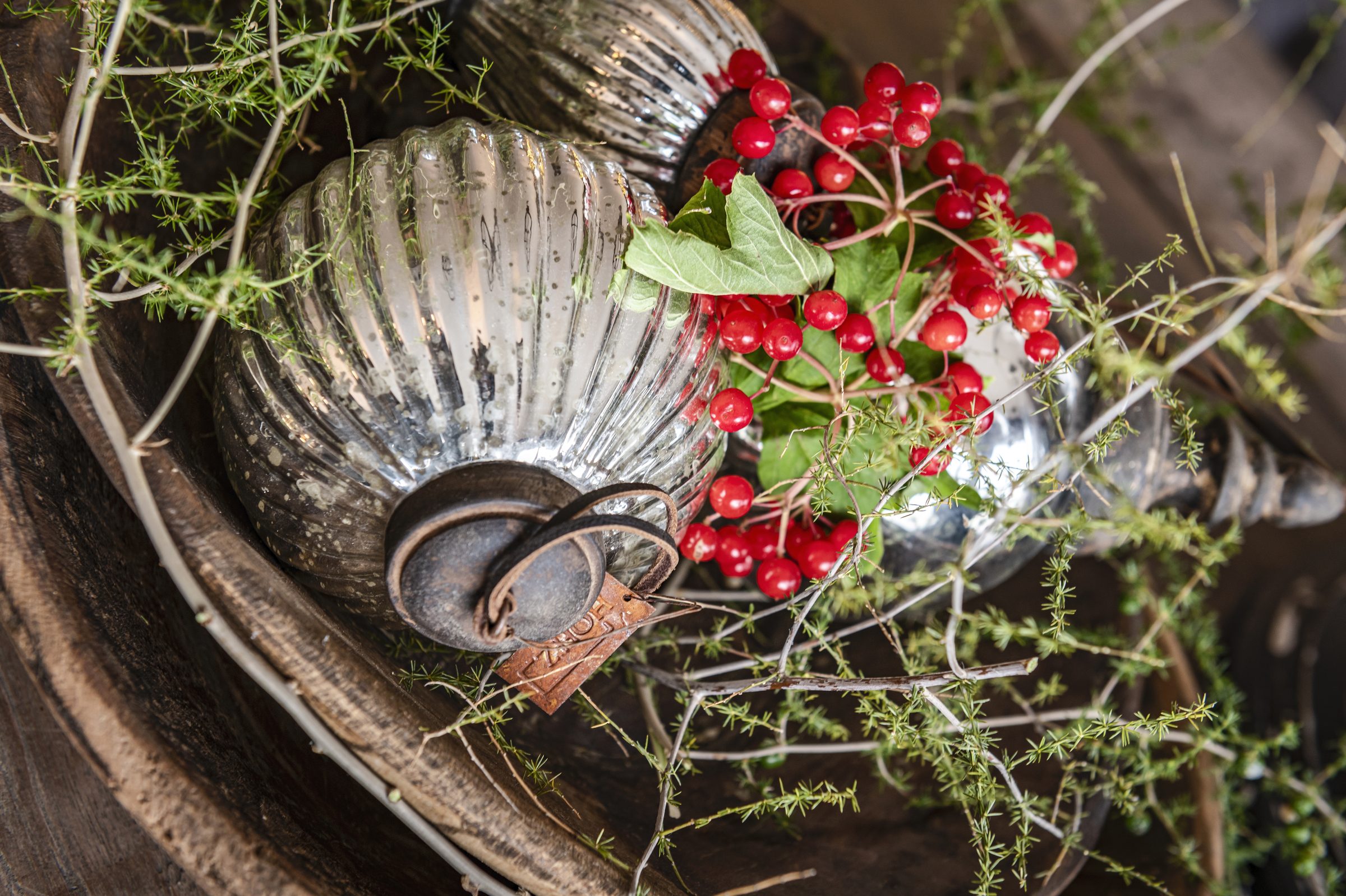 Zilveren ornamenten met rode besjes in een houten schaal
