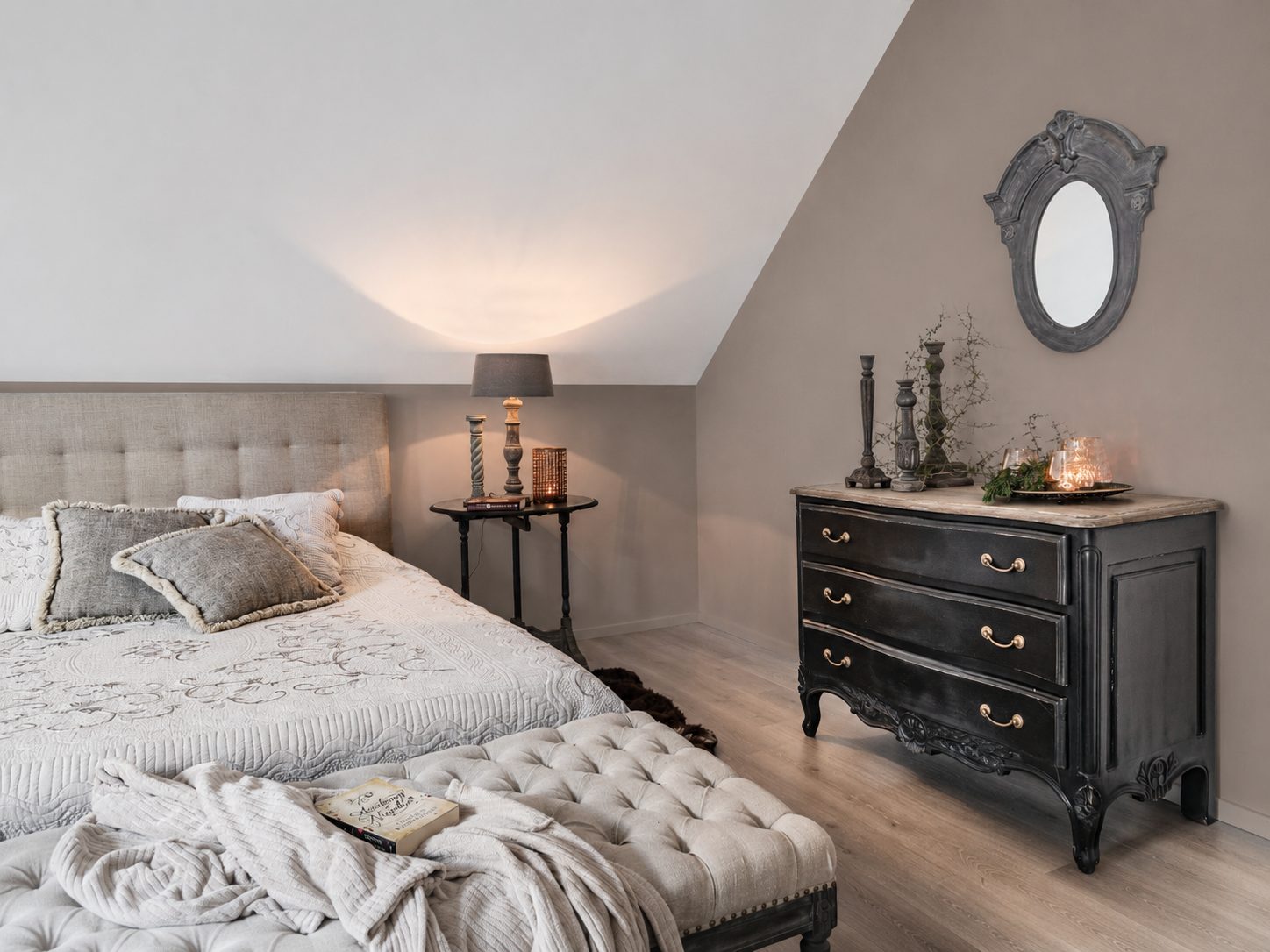 De slaapkamer met gestoffeerd bed en zwarte commode